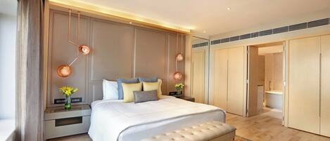 A modern bedroom with a large bed, bedside tables, a bench, and a walk-in closet.