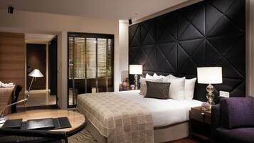 A modern hotel room with a large bed, a seating area with a table, and a separate armchair.