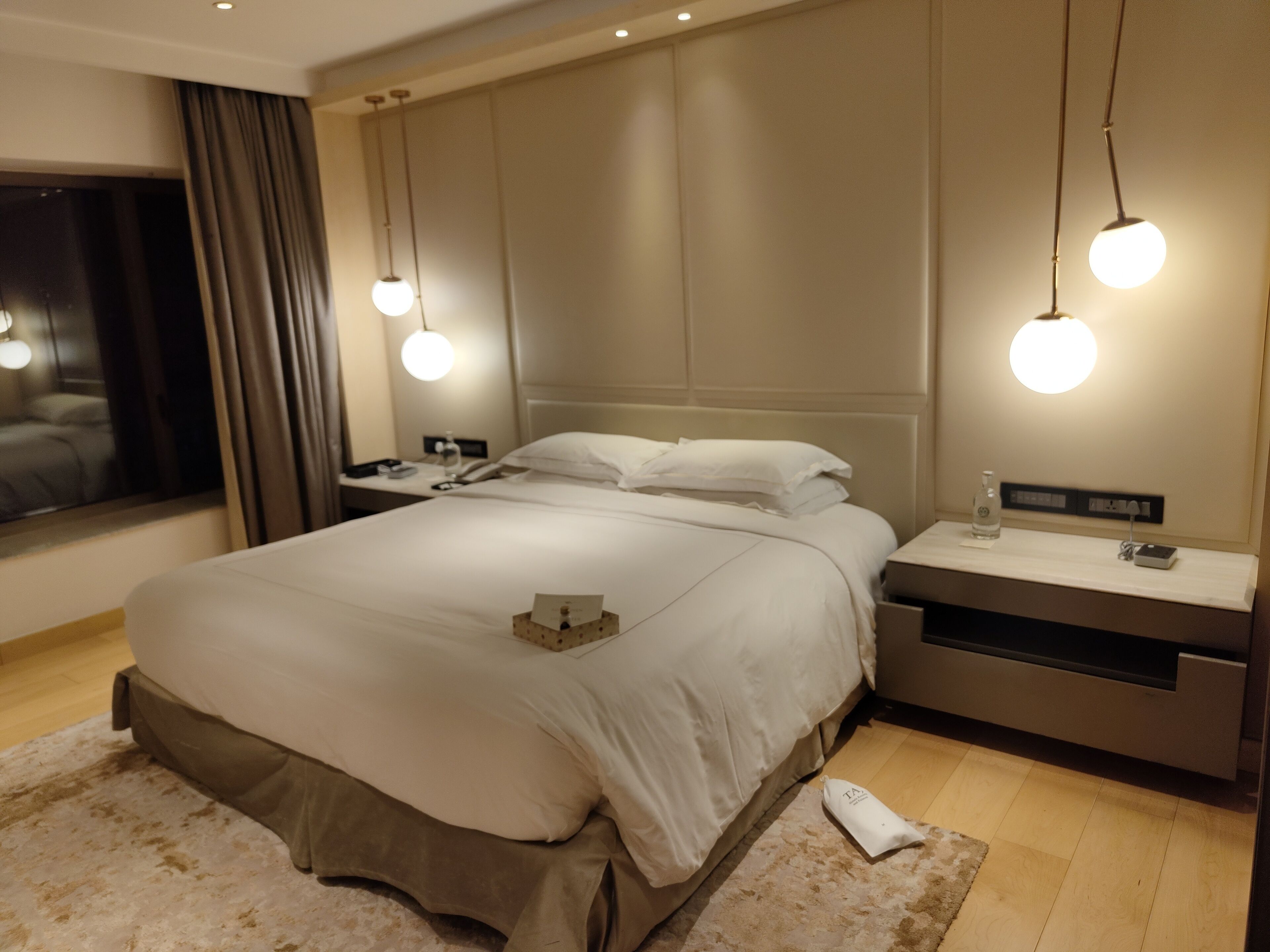 A modern hotel room with a large bed, bedside tables, and a nightstand.