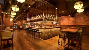 A bar area with a long counter, multiple stools, and hanging lights.