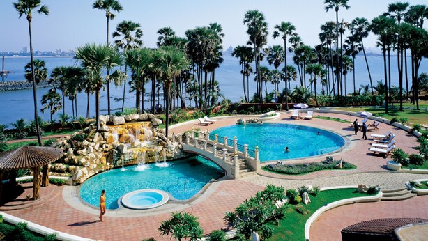 A resort pool with a waterfall, palm trees, and a view of the ocean.