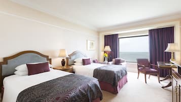 Ein Hotelzimmer mit zwei Betten, einem Schreibtisch, einem Stuhl und Blick aufs Meer.