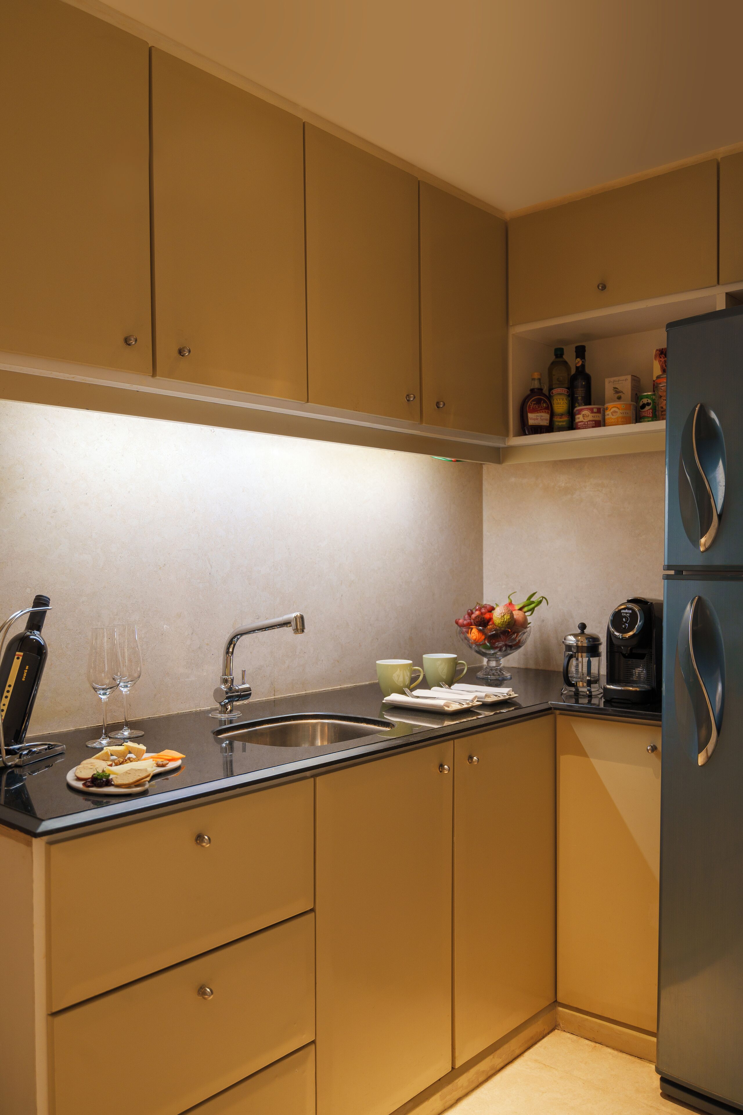 A modern kitchen with beige cabinetry, a black countertop, a sink, a coffee maker, and a fruit bowl.