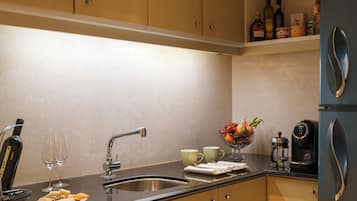 A modern kitchen with beige cabinetry, a black countertop, a sink, a coffee maker, and a fruit bowl.
