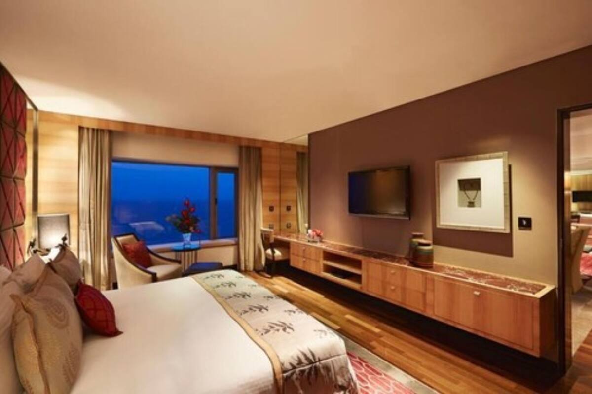 A modern hotel room with a large bed, a TV, a desk, and a view of the city at night.