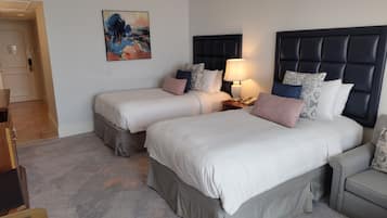 Una habitación de hotel con dos camas, una mesita de noche con lámpara, un cuadro en la pared y una puerta que da a otra habitación.