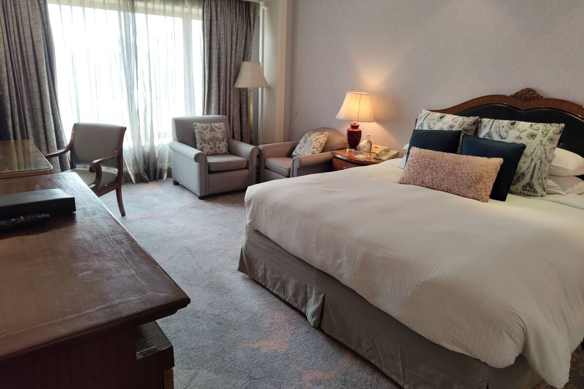 A hotel room with a large bed, two armchairs, a desk, and a TV.