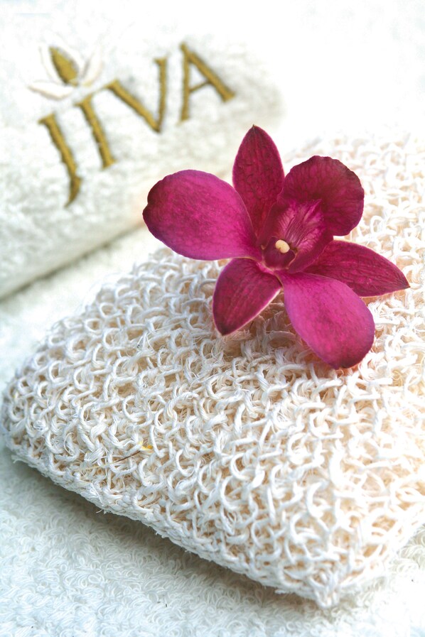 A textured white towel with a pink flower and the word "JIVA" embossed in gold.