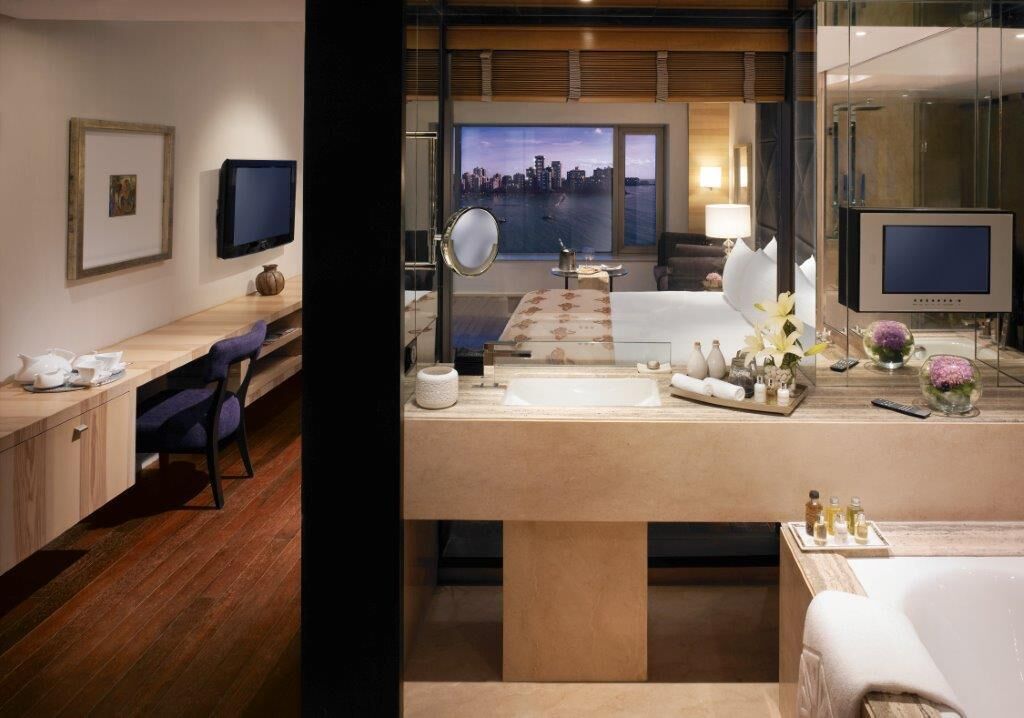 Una habitación de hotel moderna con una cama grande, un escritorio, un baño con bañera, un televisor y vistas a la ciudad.