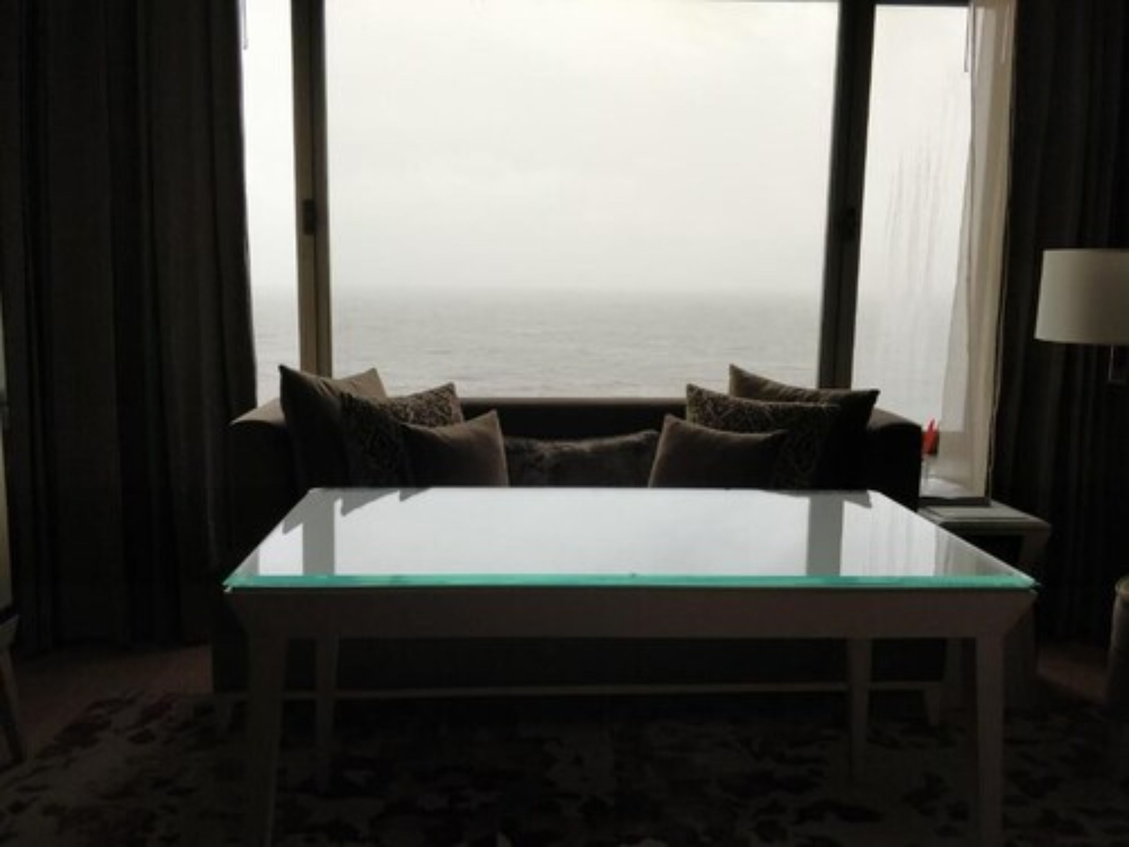 Ein Zimmer mit einem Glastisch, einer Couch mit Kissen, einer Lampe und Meerblick.
