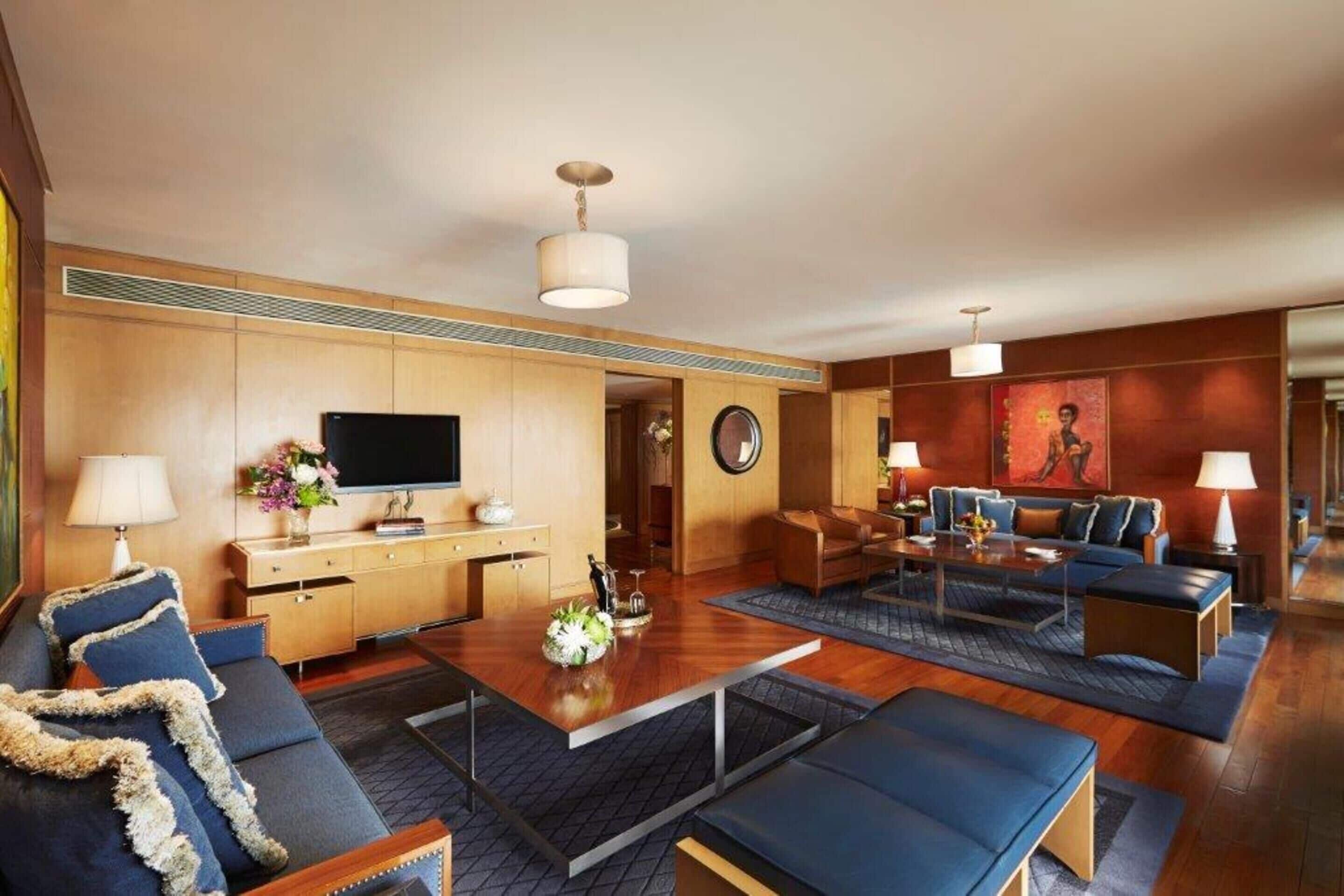 Et moderne hotelværelse med trægulv, fjernsyn, sofa, sofabord og spisebord.