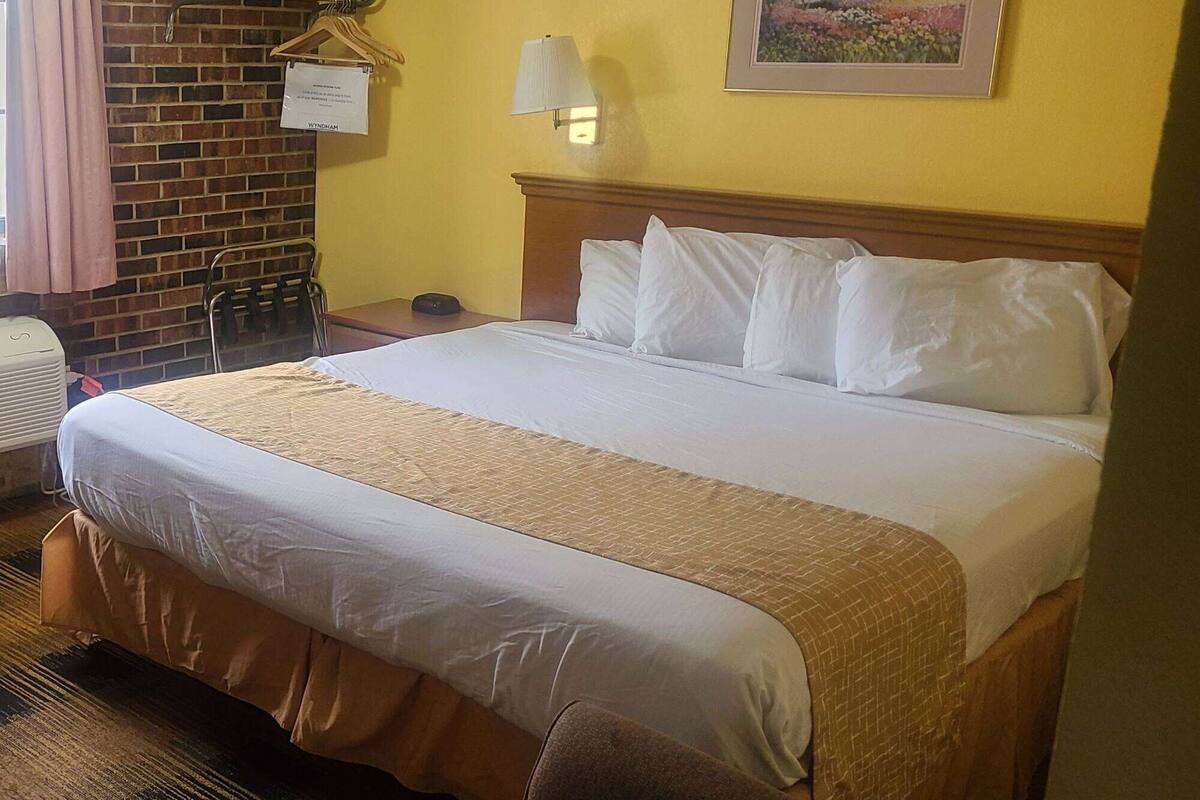 Et hotelværelse med en stor seng, et træsengegærde, et natbord, en lampe, et billede på væggen og en murstensvæg.