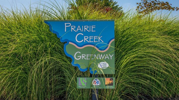 A sign for Prairie Creek Greenway with logos for MetroGreen Corridor, National Recreation Trail, and Northland Trails Route.
