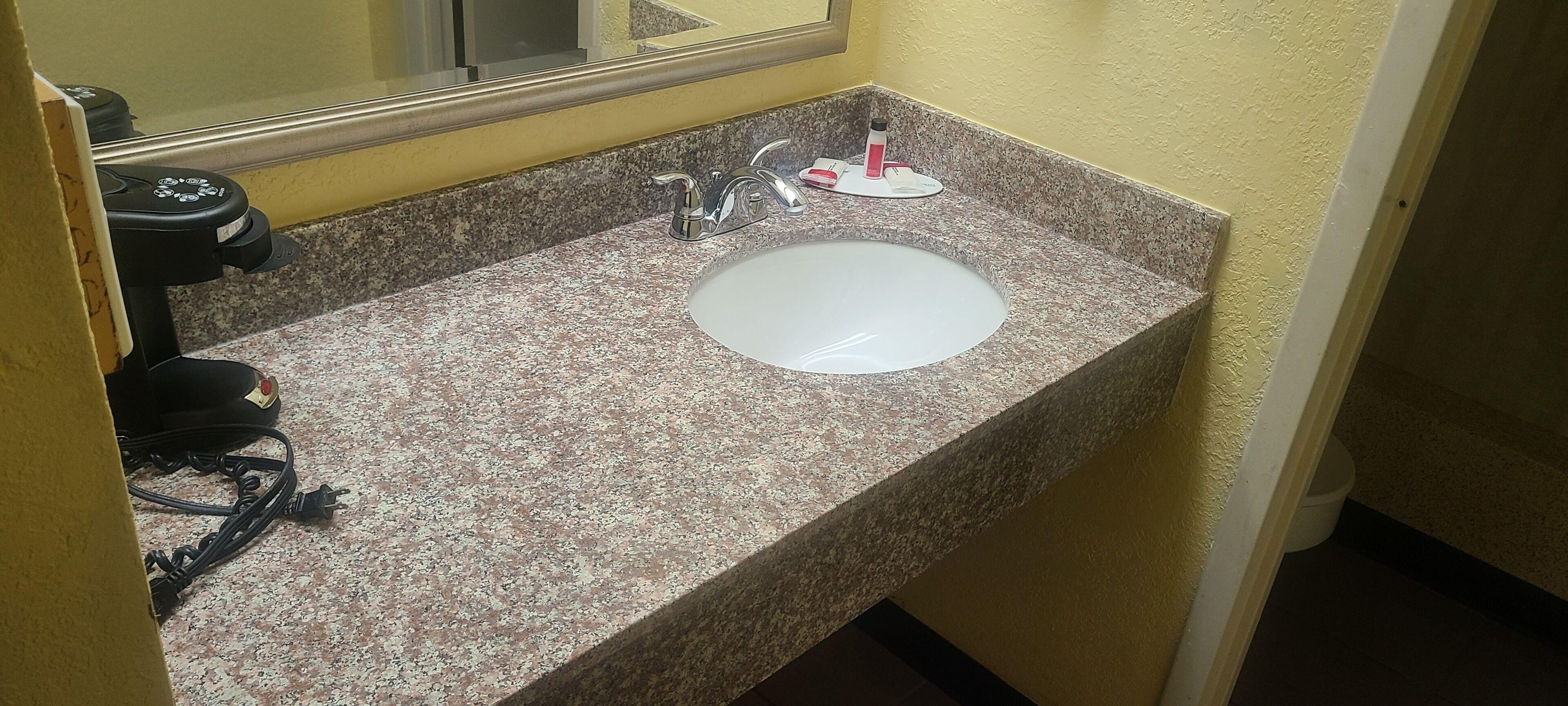 Baño con encimera de granito, un lavabo blanco, un espejo y un secador de pelo a la izquierda.