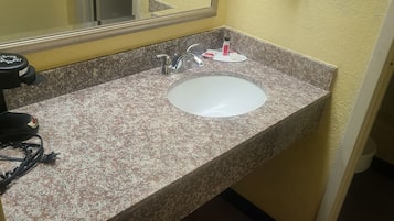 Un bagno con un piano di lavoro in granito, un lavandino bianco, uno specchio e un asciugacapelli a sinistra.