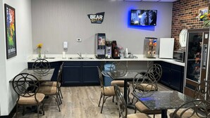 A modern kitchen with a central island, bar stools, a dining table, and a TV mounted on the wall.