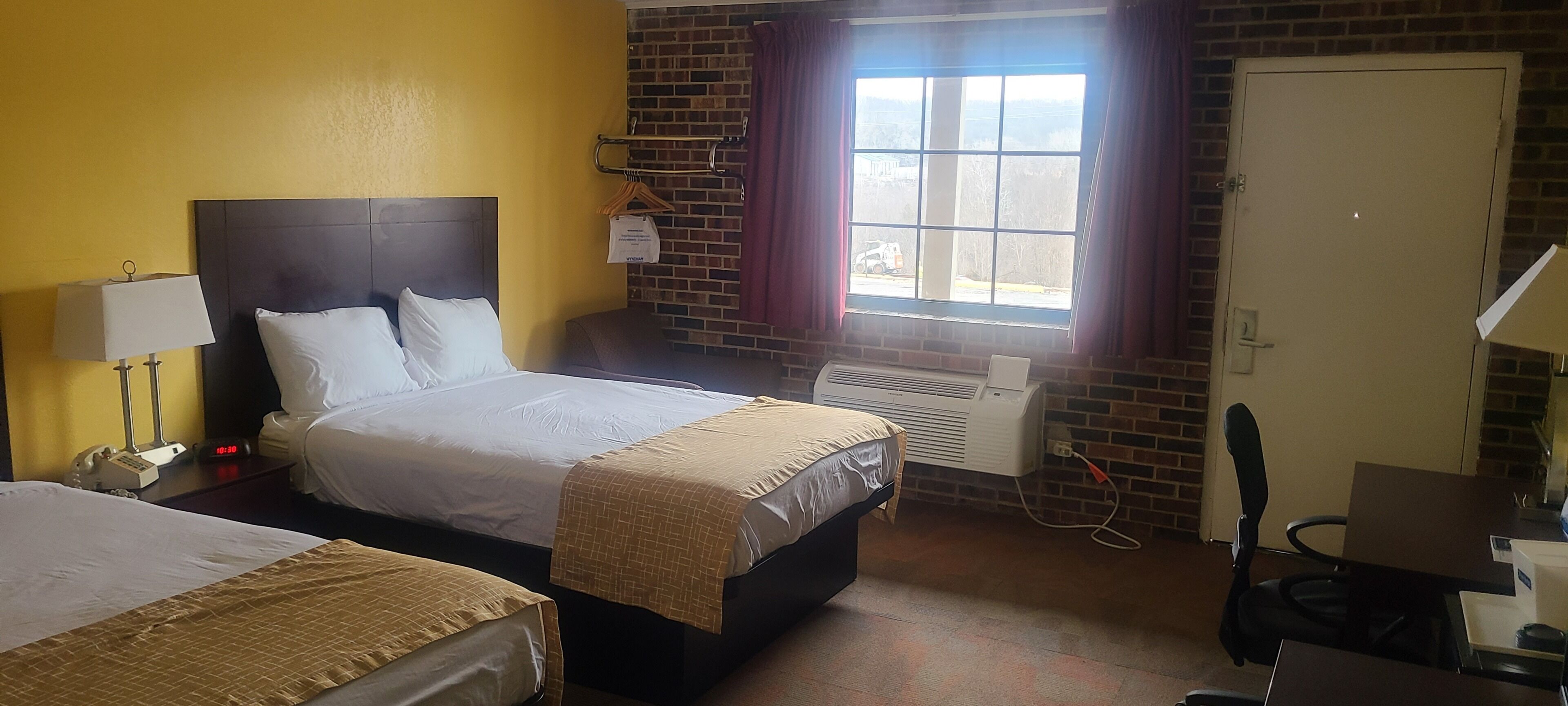 A hotel room with two beds, a desk, a chair, a window with curtains, a heater, and a door.