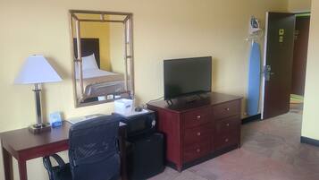A hotel room with a desk, a chair, a television, a dresser, a mirror, and a door with a sign.