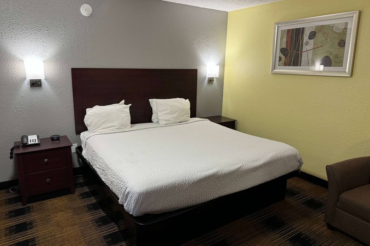 Et hotelværelse med en stor seng, et natbord med en telefon og et billede på væggen.
