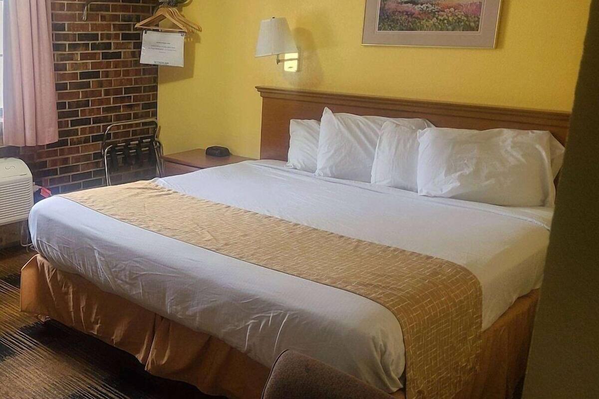 Et hotelværelse med en stor seng, en murstensvæg, et træsengegærde, et natbord, en lampe og et billede på væggen.