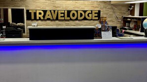A reception desk with a 'TRAVELodge' sign, a bear mascot, and a clock.