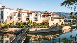 A waterfront hotel with a reflective pool, a pedestrian bridge, and a view of mountains in the background. - Harbor View Inn (Santa Barbara)