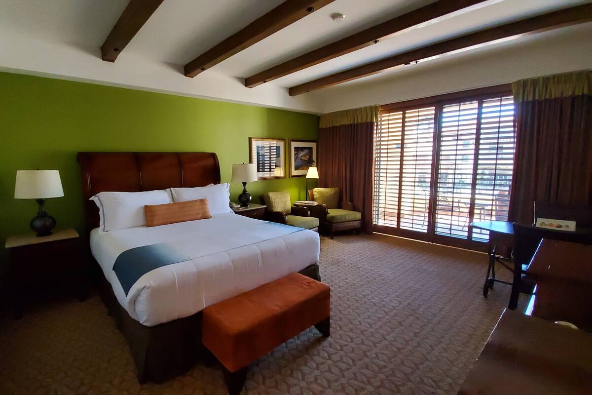 A hotel room with a large bed, a nightstand, a chair, a desk, and a window with blinds.
