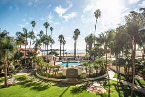 A resort with a swimming pool surrounded by palm trees, a beach view, and a well-maintained lawn. - Harbor View Inn (Santa Barbara)