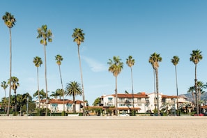 A beachfront hotel with multiple floors, palm trees, and a clear sky.