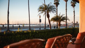A seaside patio with wicker chairs, a view of the marina, and palm trees. - Harbor View Inn (Santa Barbara)