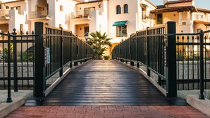 A bridge leading to a row of white buildings with balconies, a palm tree, and a brick pathway. - Harbor View Inn (Santa Barbara)
