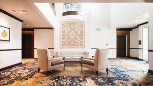A spacious lobby with a high ceiling, a central seating area with two armchairs and a small table, a patterned wall, and a wooden floor. - Harbor View Inn (Santa Barbara)