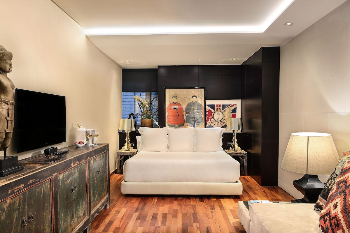 A modern bedroom with a large bed, a flat-screen TV, a wooden cabinet, and artwork on the walls.