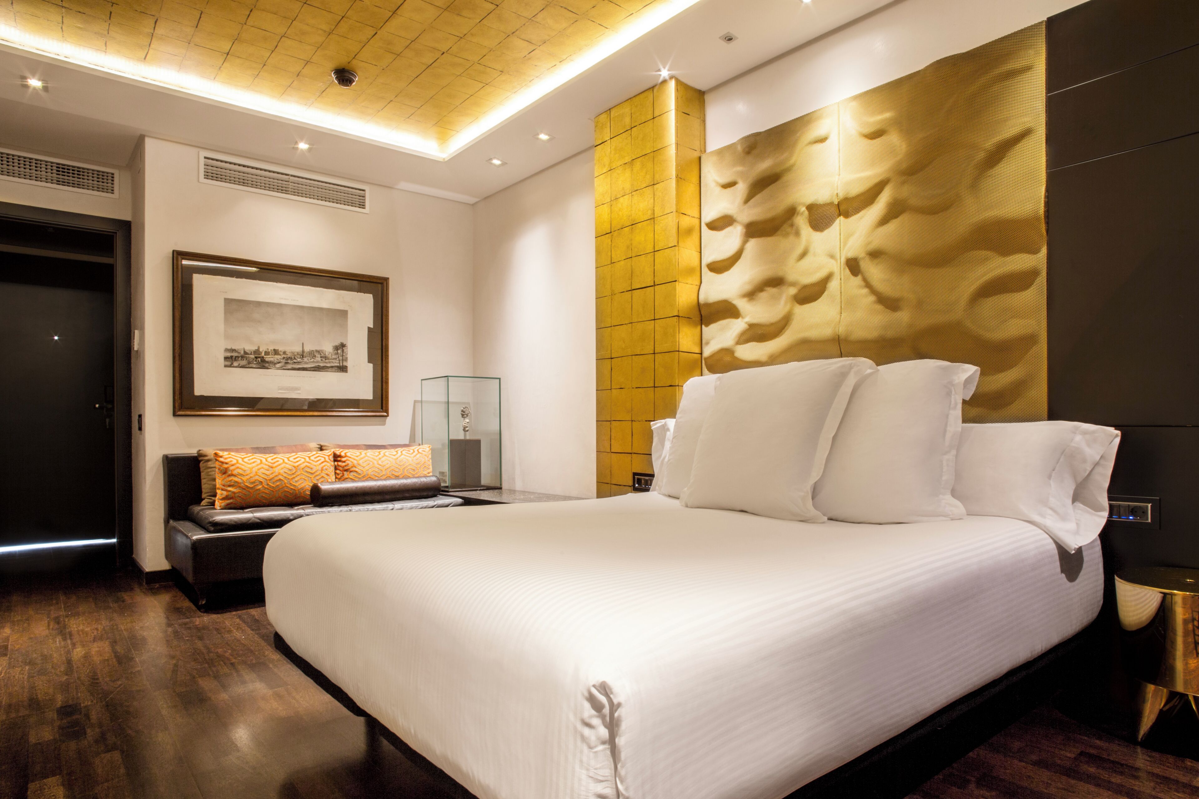 A modern hotel room with a large bed, a framed picture on the wall, and a unique textured wall design.