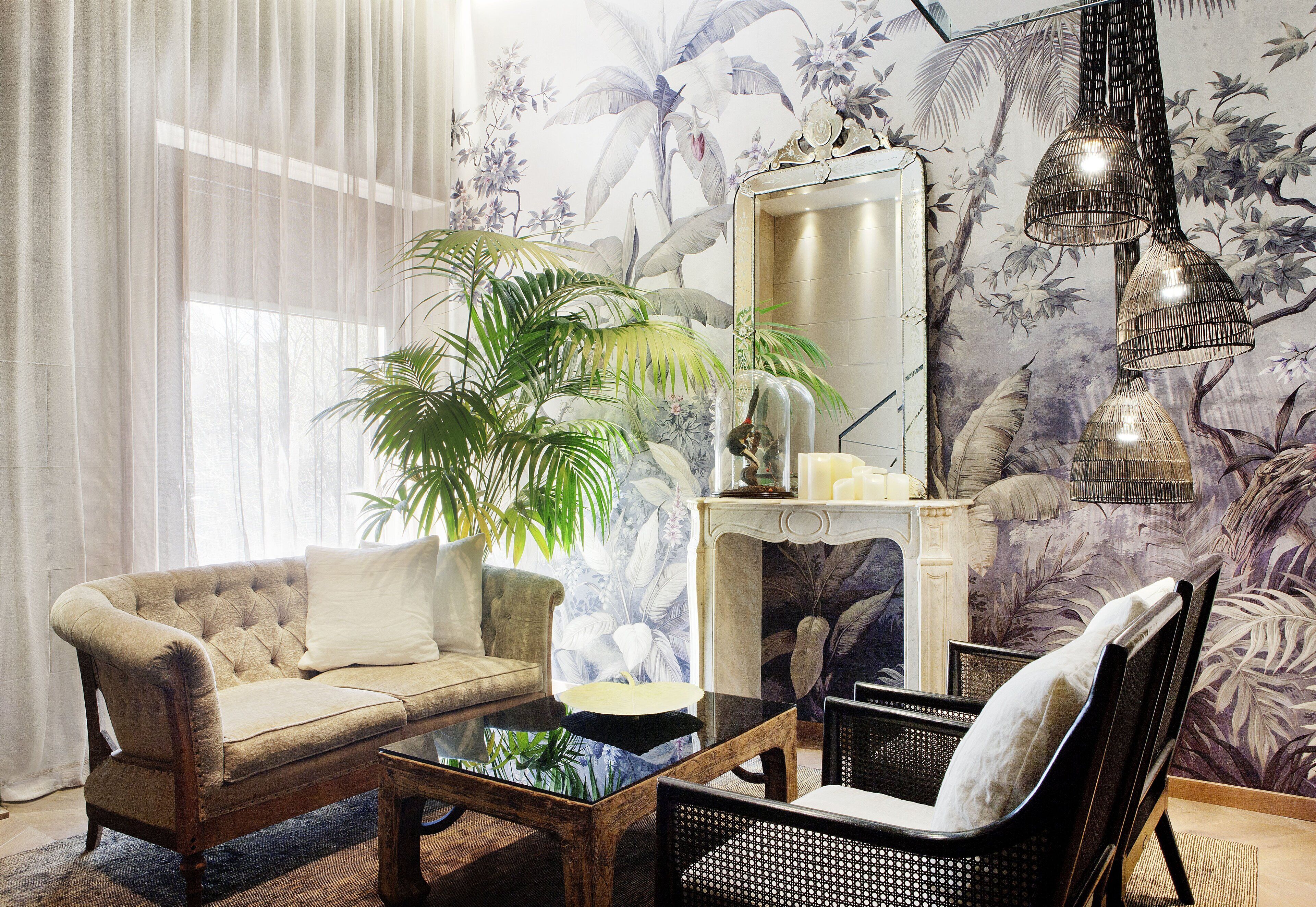 A living room with a sofa, armchairs, a coffee table, a large potted plant, a fireplace, and a wall with a floral mural.