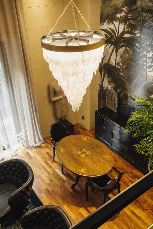 Una habitación con una mesa redonda de madera, sillas tapizadas de color negro, una lámpara de araña colgante y una planta en maceta.