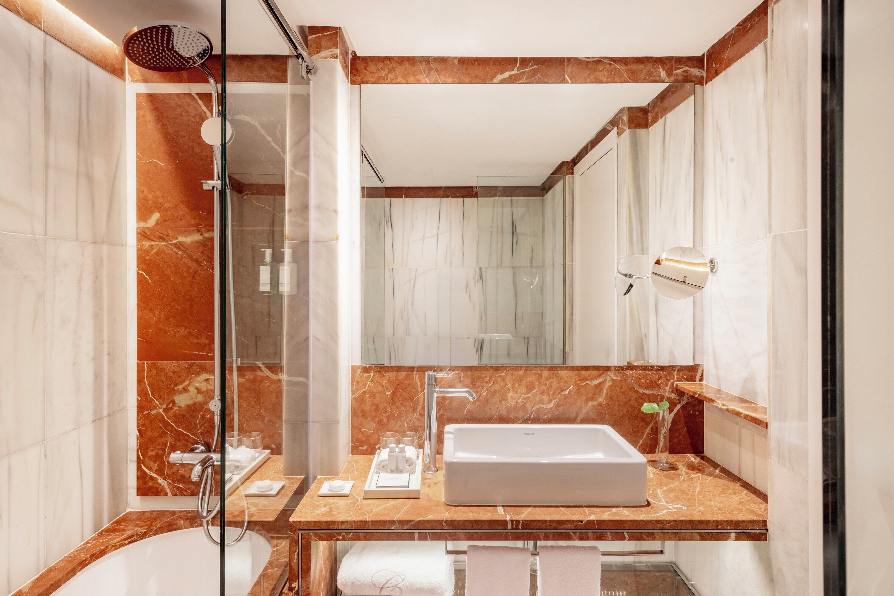 Un baño moderno con ducha envuelta en vidrio, un lavamanos grande y paredes de mármol.