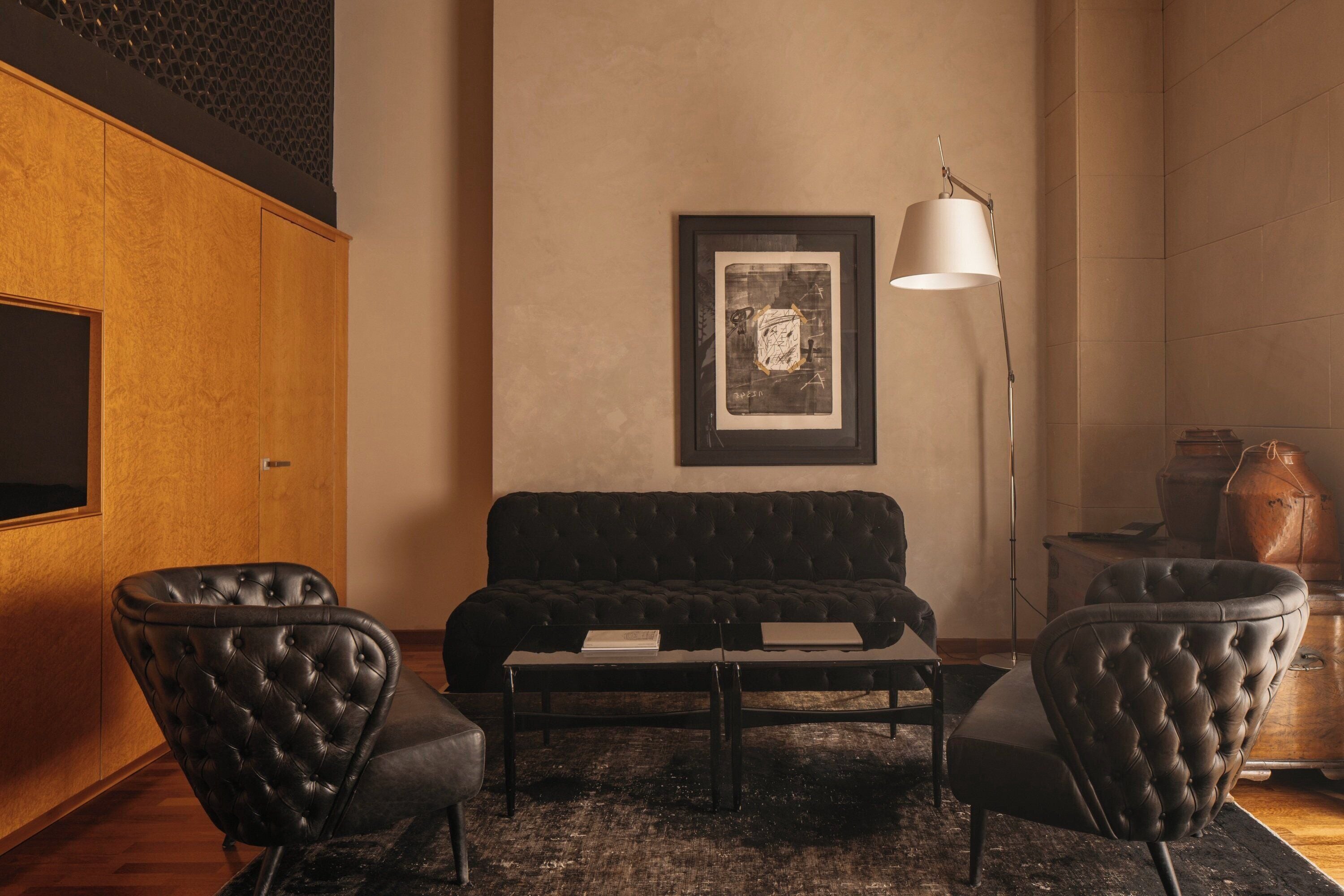 A modern living room with a dark-colored sofa, two leather armchairs, a coffee table, and a framed artwork on the wall.