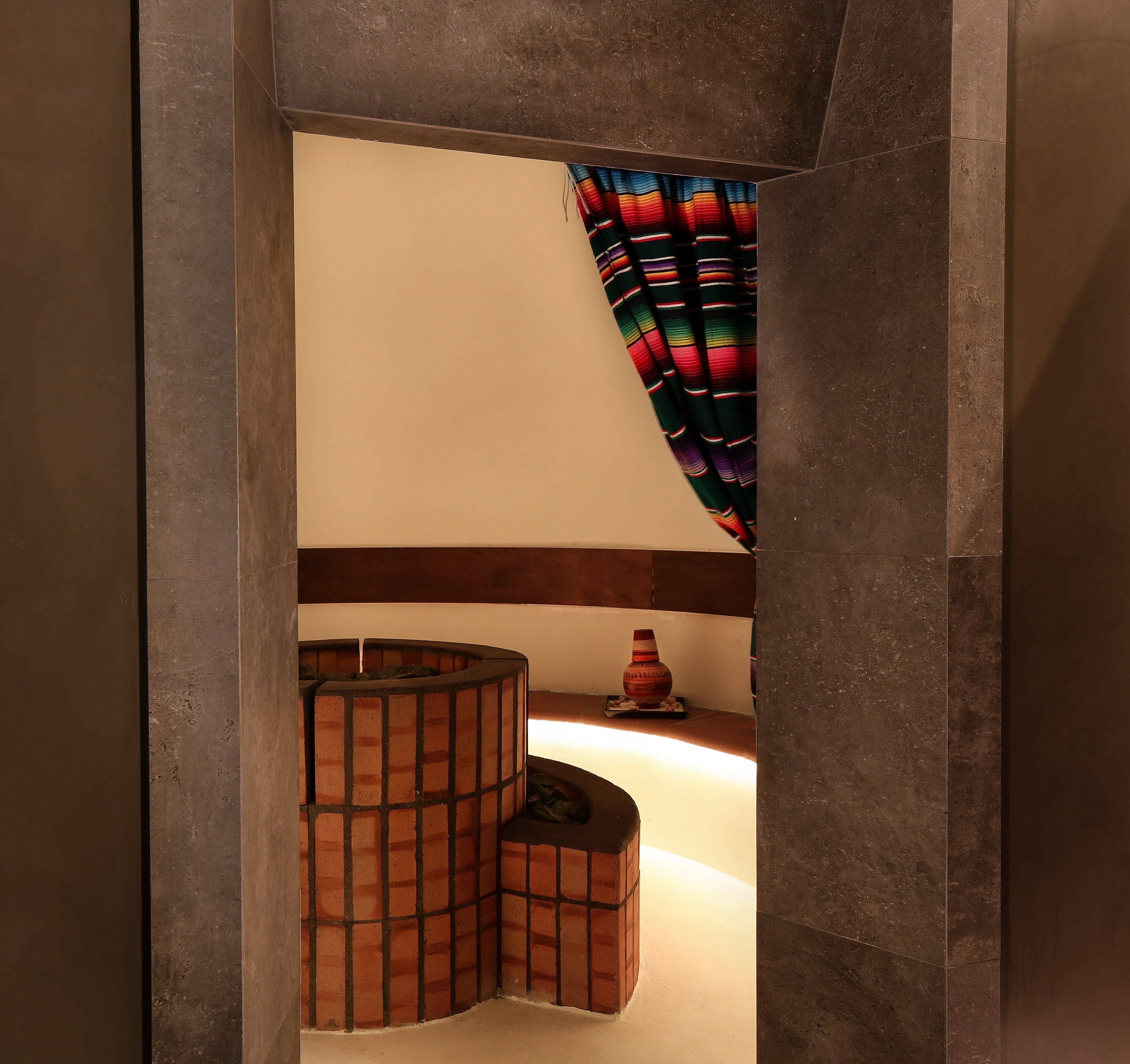 Ein modernes Interieur mit einer gewölbten Ziegelstruktur, einer kleinen Ablage mit dekorativer Vase und einem farbenfrohen, gestreiften Vorhang.