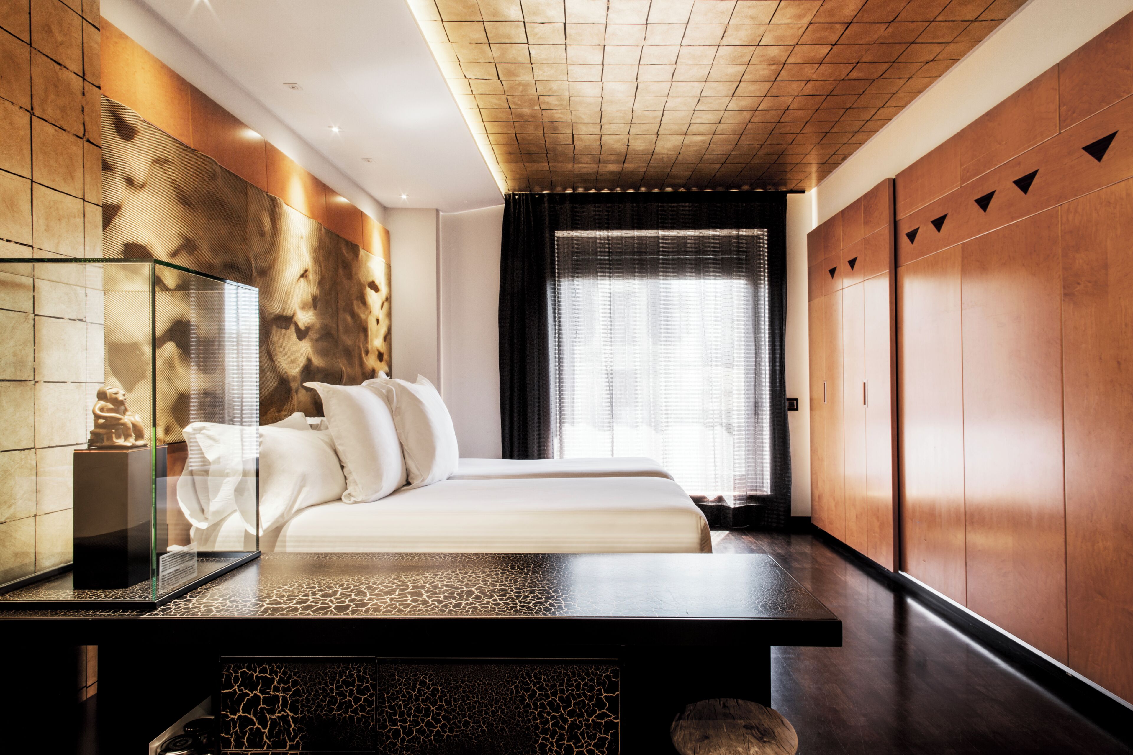 A modern hotel room with a bed, a glass display case, and a wooden wardrobe.