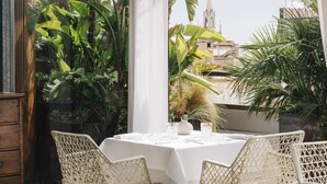 A covered outdoor dining area with a table and chairs, surrounded by lush plants and a view of buildings. - Claris Hotel & Spa 5*GL, a Small Luxury Hotels of the World (Barcelona)