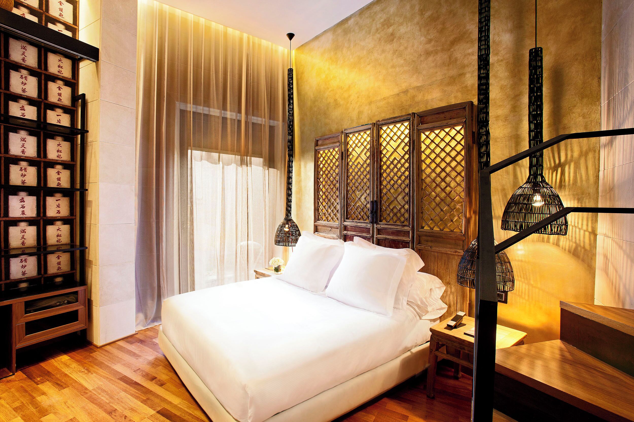 A neatly arranged hotel room with a bed, bedside table, and a shelf with items.