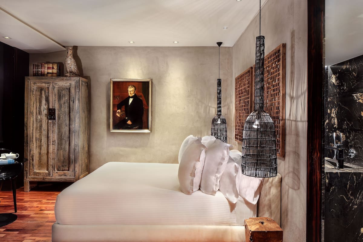A bedroom with a large bed, a wooden cabinet, a painting, and a modern pendant light.