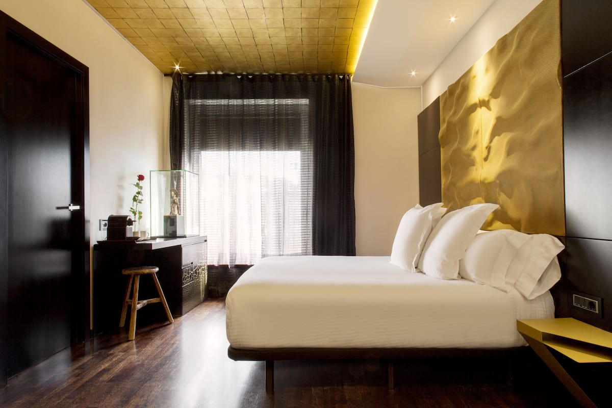 A modern bedroom with a large bed, a desk with a chair, and a window with curtains.