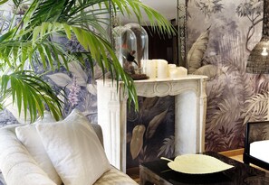 Classic decor with a white armchair, console table, and floral wallpaper, complemented by a large potted plant.