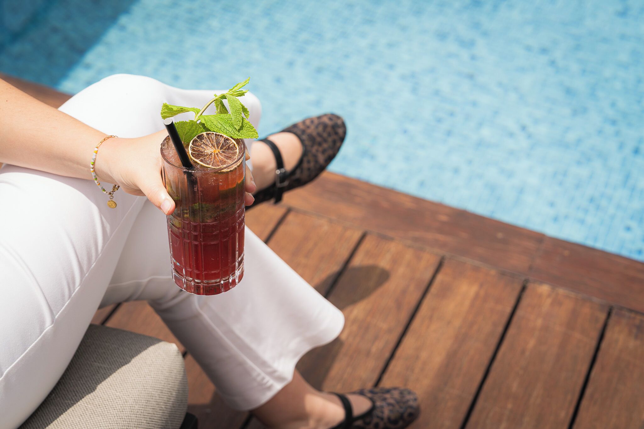 A person holding a glass with a drink, sitting by a pool.