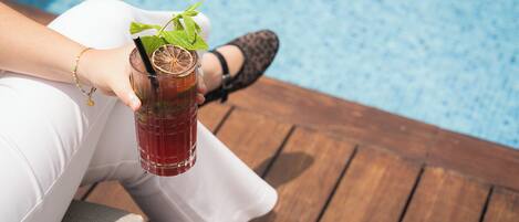 A person holding a glass with a drink, sitting by a pool.