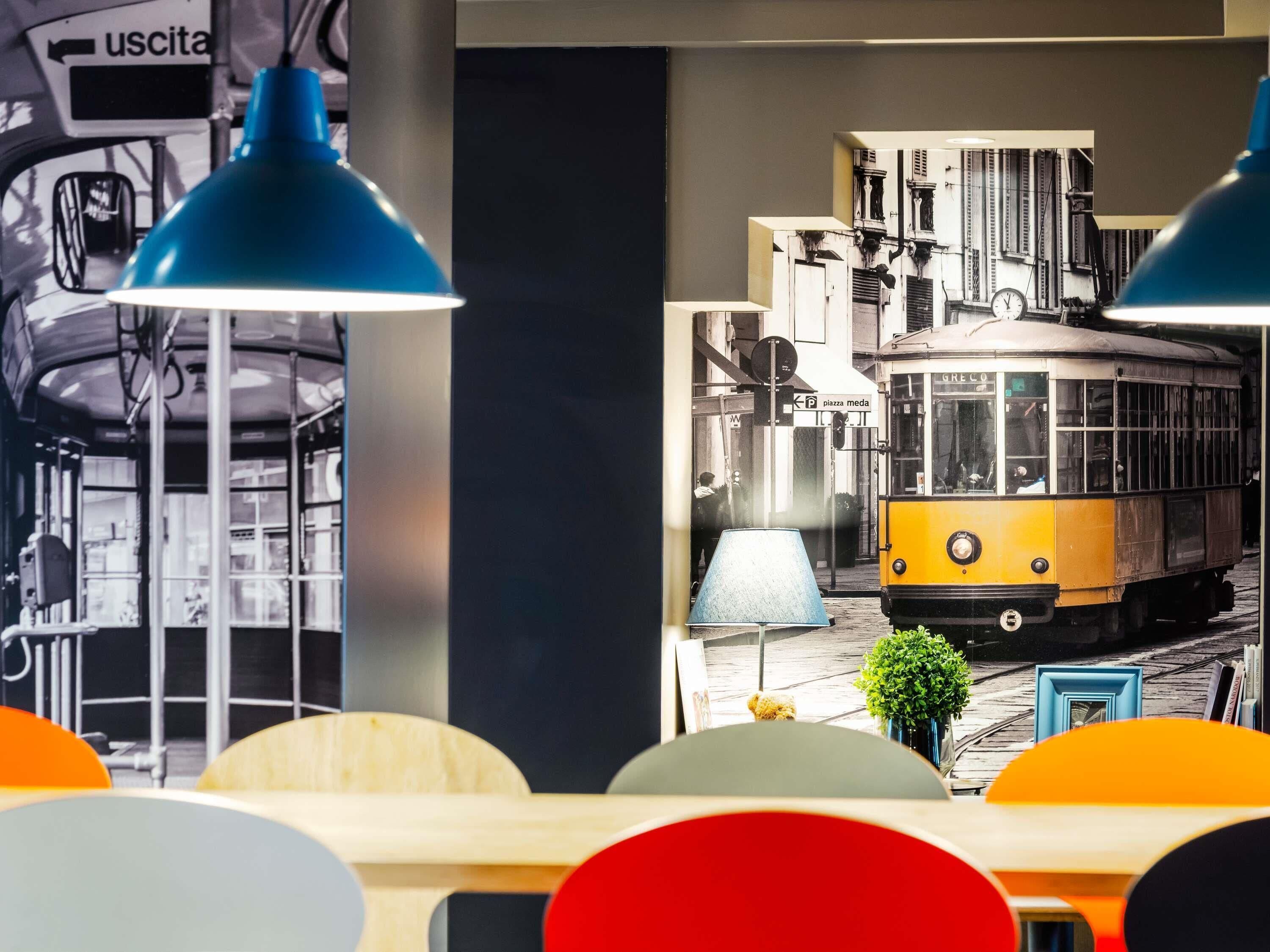 A room with a large wall mural of a vintage tram, a wooden table, and blue pendant lights.