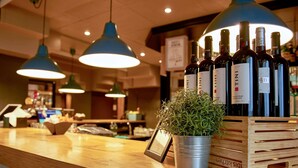 Zona de bar con mostrador de madera, lámparas colgantes azules, una planta en maceta y un cesto con botellas de vino.
