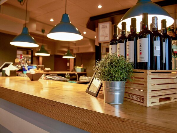 A bar area with wooden counter, hanging blue pendant lights, a potted plant, and a crate of wine bottles.
